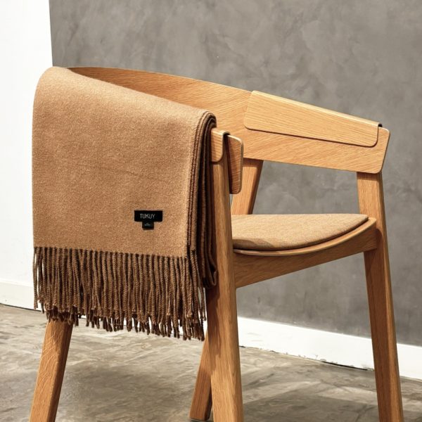 Camel baby alpaca wool blanket folded over a modern wooden chair with soft fringes – sustainable luxury throw made in Peru