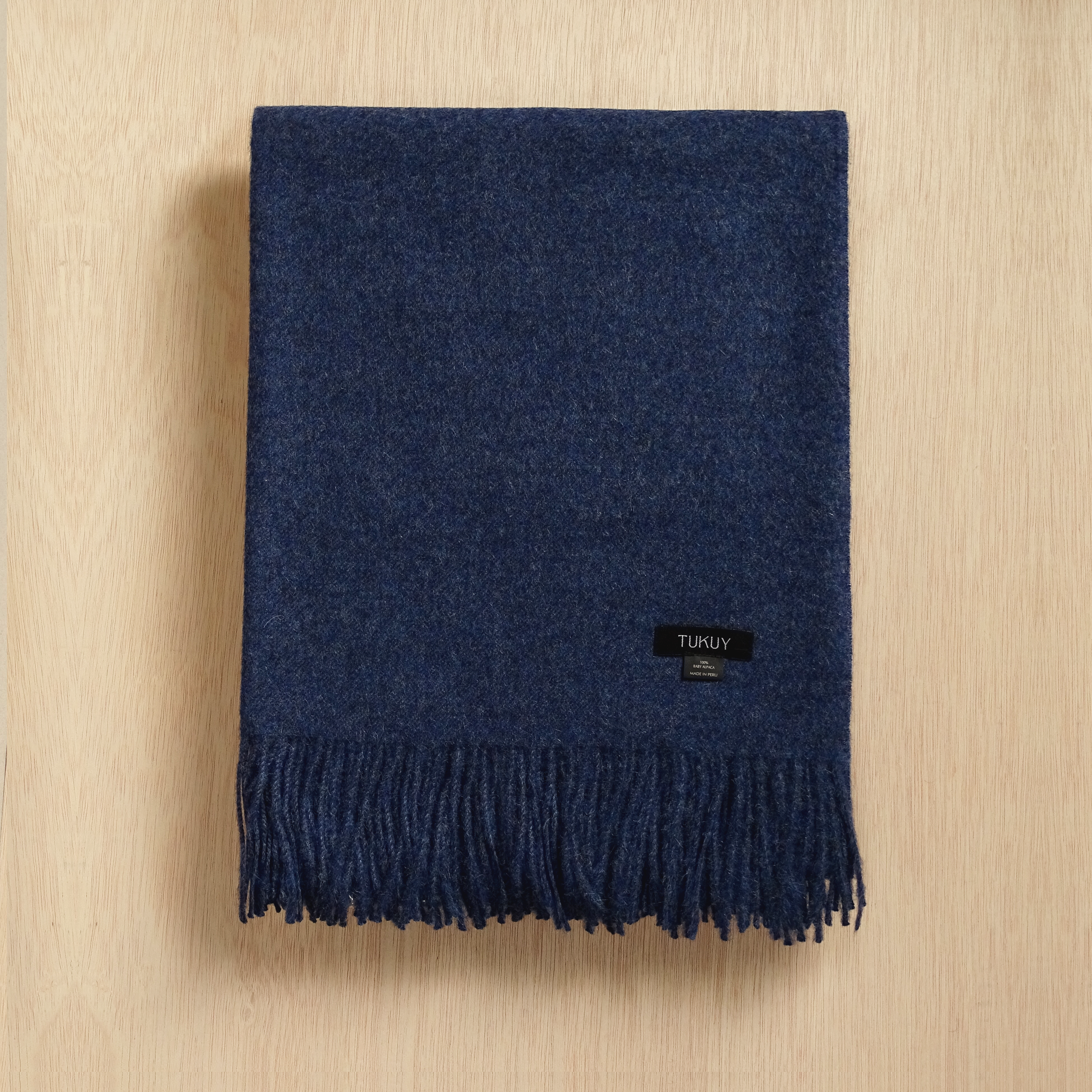 blue alpaca blanket by Tukuy in navy blue placed on top of a wooden background