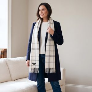 Woman wearing a white and gray check alpaca scarf with a navy coat, cream sweater, and blue jeans, showcasing how the timeless checked design pairs effortlessly with both neutral and classic colors.