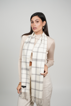 Woman wearing a white and gray check alpaca scarf with a timeless windowpane pattern, showcasing its elegant drape, soft alpaca wool texture, and versatile neutral color palette.