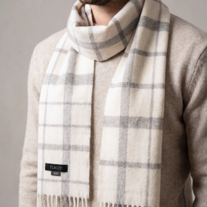 Man wearing a white and gray check alpaca scarf paired with a light knit sweater, highlighting the scarf's classic heritage-inspired pattern and refined winter styling.
