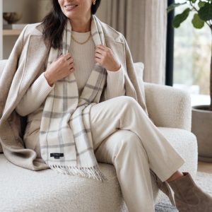 Woman wearing a white and gray check alpaca scarf with cream knitwear and ivory trousers, showcasing how the timeless checked pattern complements soft neutral tones for an elegant winter outfit.