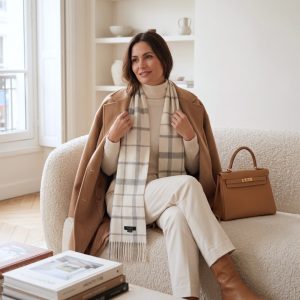 Woman styling a white and gray check alpaca scarf with a camel coat and cream clothing, demonstrating a sophisticated combination of classic checks and warm neutral colors.