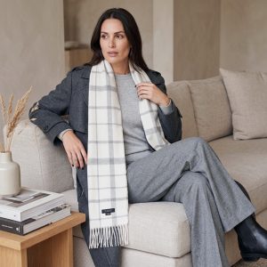 Woman wearing a white and gray check alpaca scarf with a charcoal gray suit, highlighting the versatility of the heritage-inspired pattern with modern tailored styling.