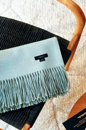 Soft baby green baby alpaca blanket draped over a chair showcasing its luxurious texture and fringe details