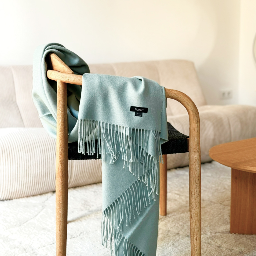 Green alpaca blanket from Tukuy draped over a chair in a cozy living room with a beige sofa