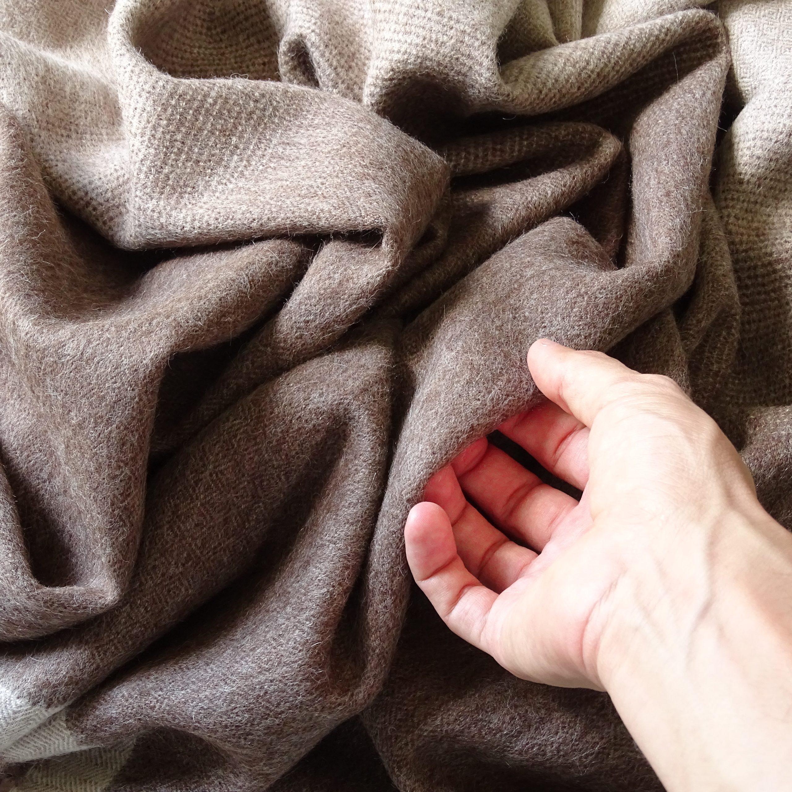 tocando con la mano la suavidad de una manta de alpaca marrón y beige de Tukuy