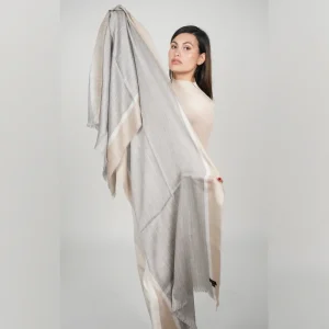 woman holding the alpaca shawl in beige and gray to show the design