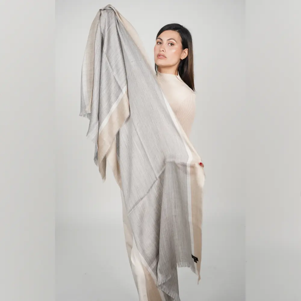 woman holding the alpaca shawl in beige and gray to show the design