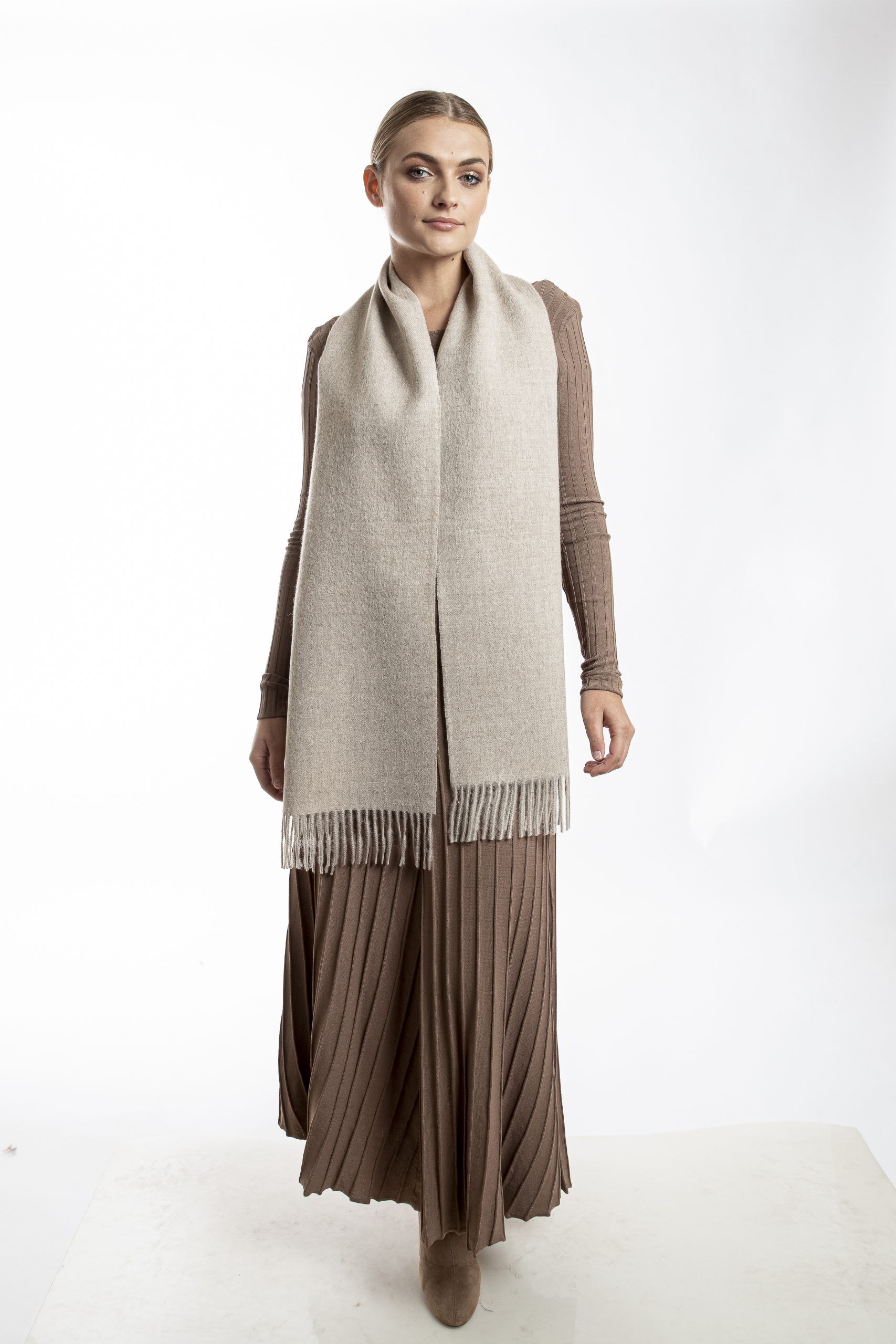 Woman wearing an oatmeal baby alpaca scarf from Tukuy with fringed edges, styled over a beige dress