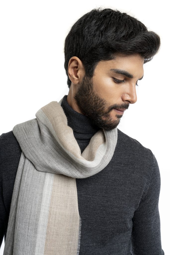 Man wearing a lightweight striped baby alpaca shawl from Tukuy in shades of grey and beige, styled over a dark turtleneck and brown trousers