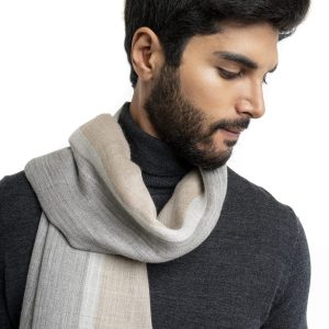Man wearing a lightweight striped baby alpaca shawl from Tukuy in shades of grey and beige, styled over a dark turtleneck and brown trousers