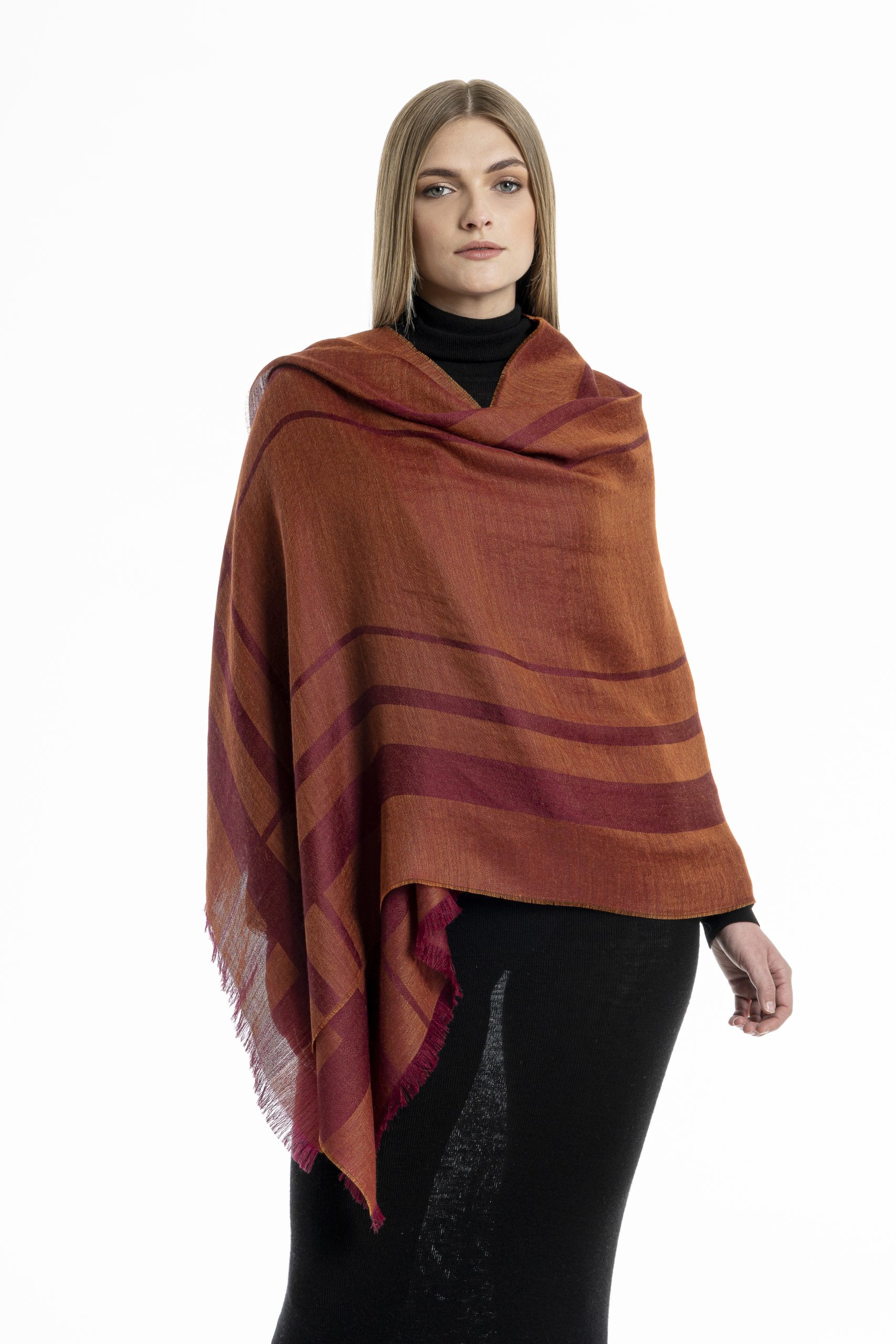 Woman wearing a lightweight burgundy striped shawl made from baby alpaca and silk, styled over a black outfit against a white background.