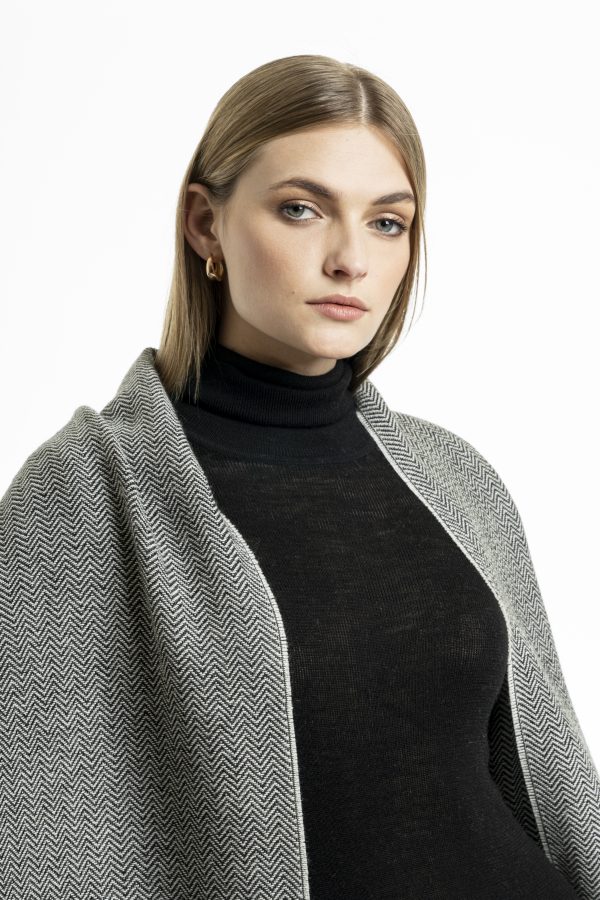 Woman wearing a dark grey baby alpaca shawl with light grey stripes from Tukuy, styled over a light black outfit