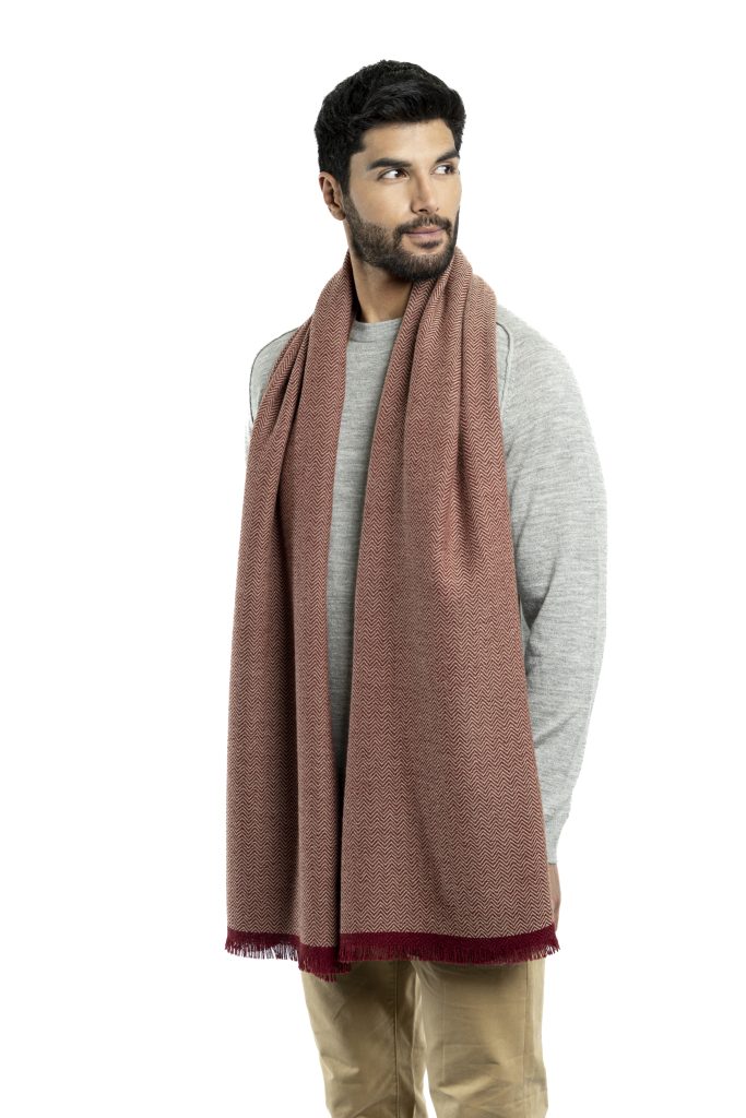 Man wearing a red herringbone-patterned baby alpaca wool scarf from Tukuy with burgundy fringed edges, styled over a light grey sweater