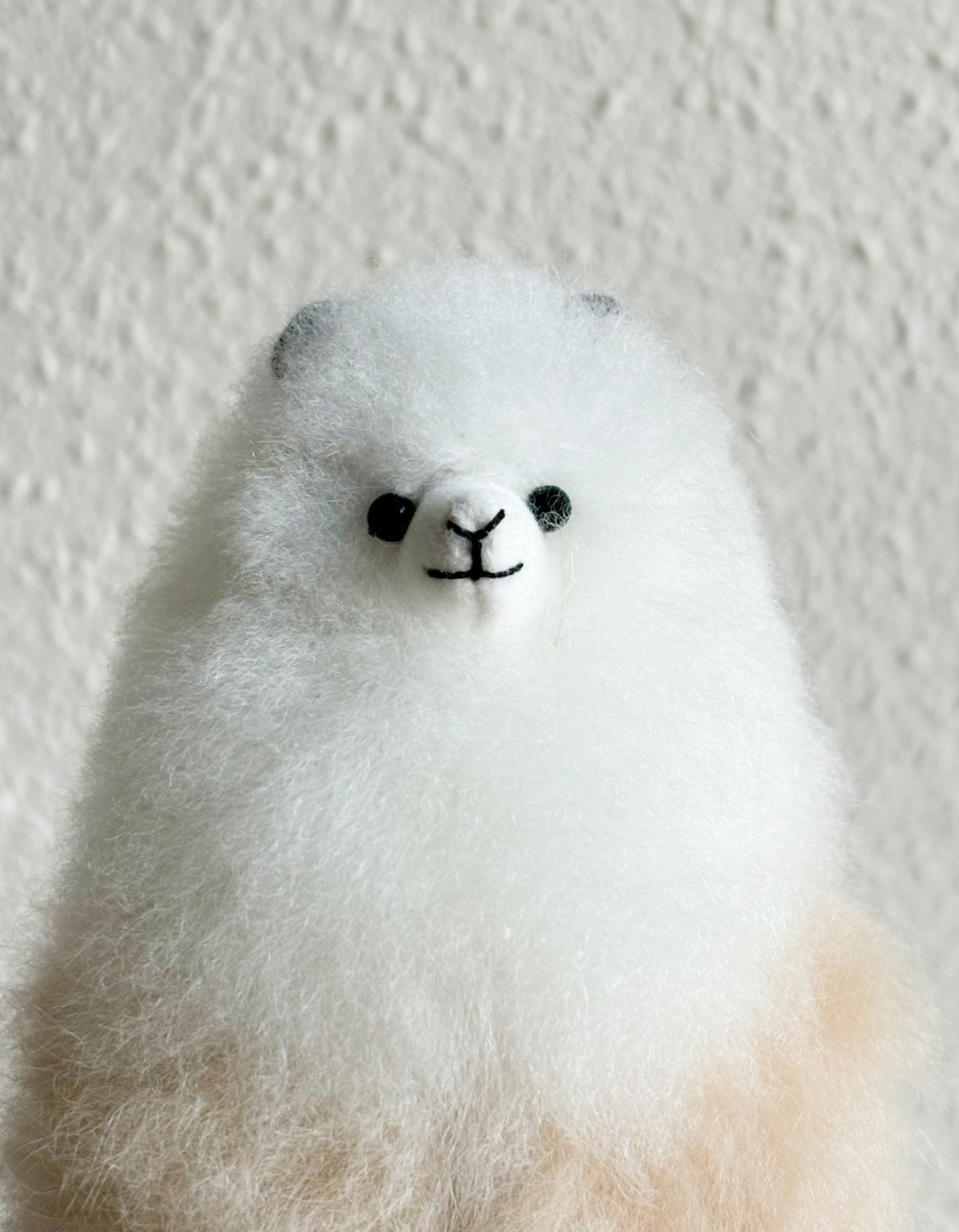 Handmade alpaca plush made from natural baby alpaca fur by Tukuy, featuring soft cream and white tones with black stitched eyes and ears