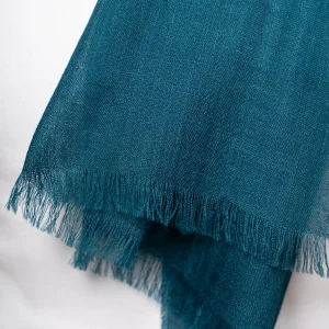 Woman wearing a gradient blue alpaca shawl from Tukuy, styled over a white outfit and posed against a soft beige background.