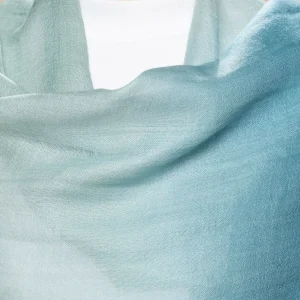 Woman wearing a gradient blue alpaca shawl from Tukuy, styled over a white outfit and posed against a soft beige background.