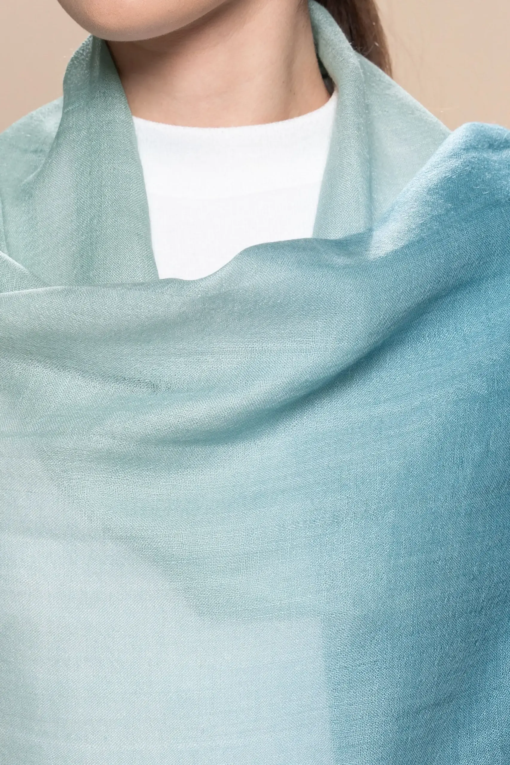 Woman wearing a gradient blue alpaca shawl from Tukuy, styled over a white outfit and posed against a soft beige background.