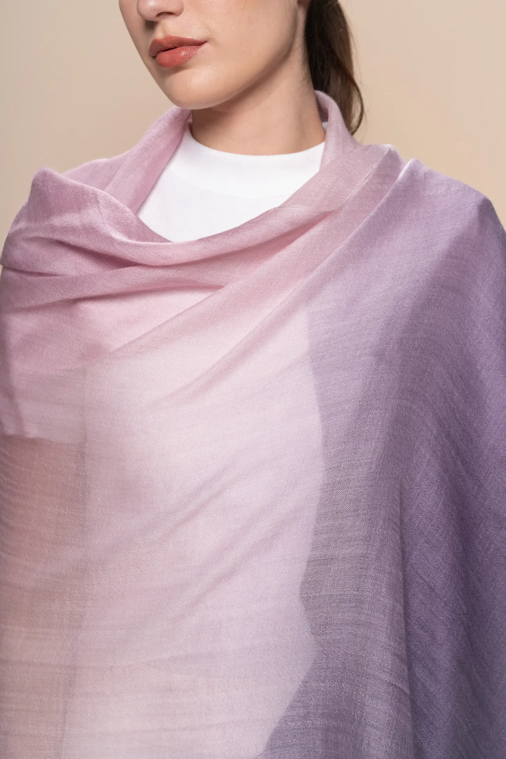 close up of a woman wearing a gradient pink-to-purple baby alpaca wool scarf from Tukuy, styled over a white outfit and posed against a soft beige background.