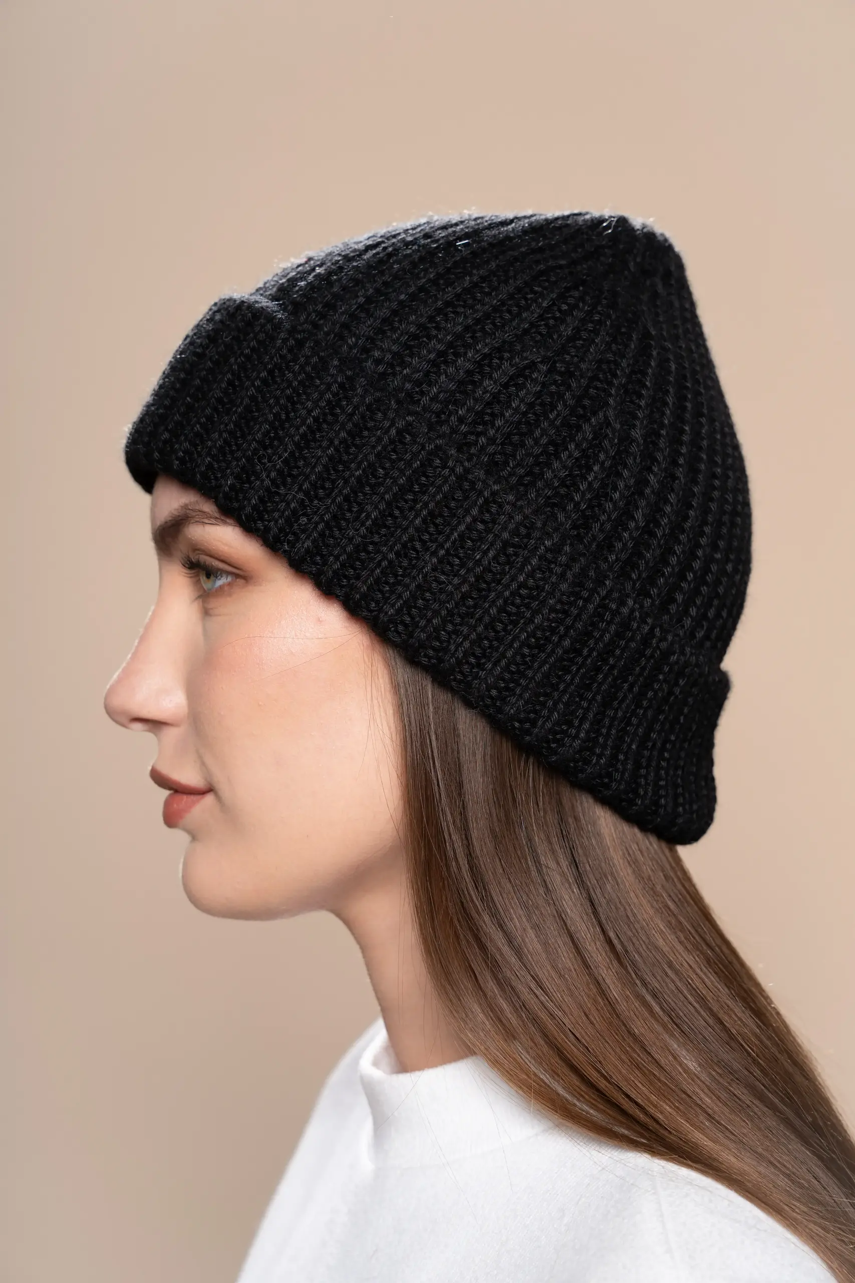 Woman wearing a black ribbed baby alpaca wool beanie from Tukuy, shown in profile against a neutral background.