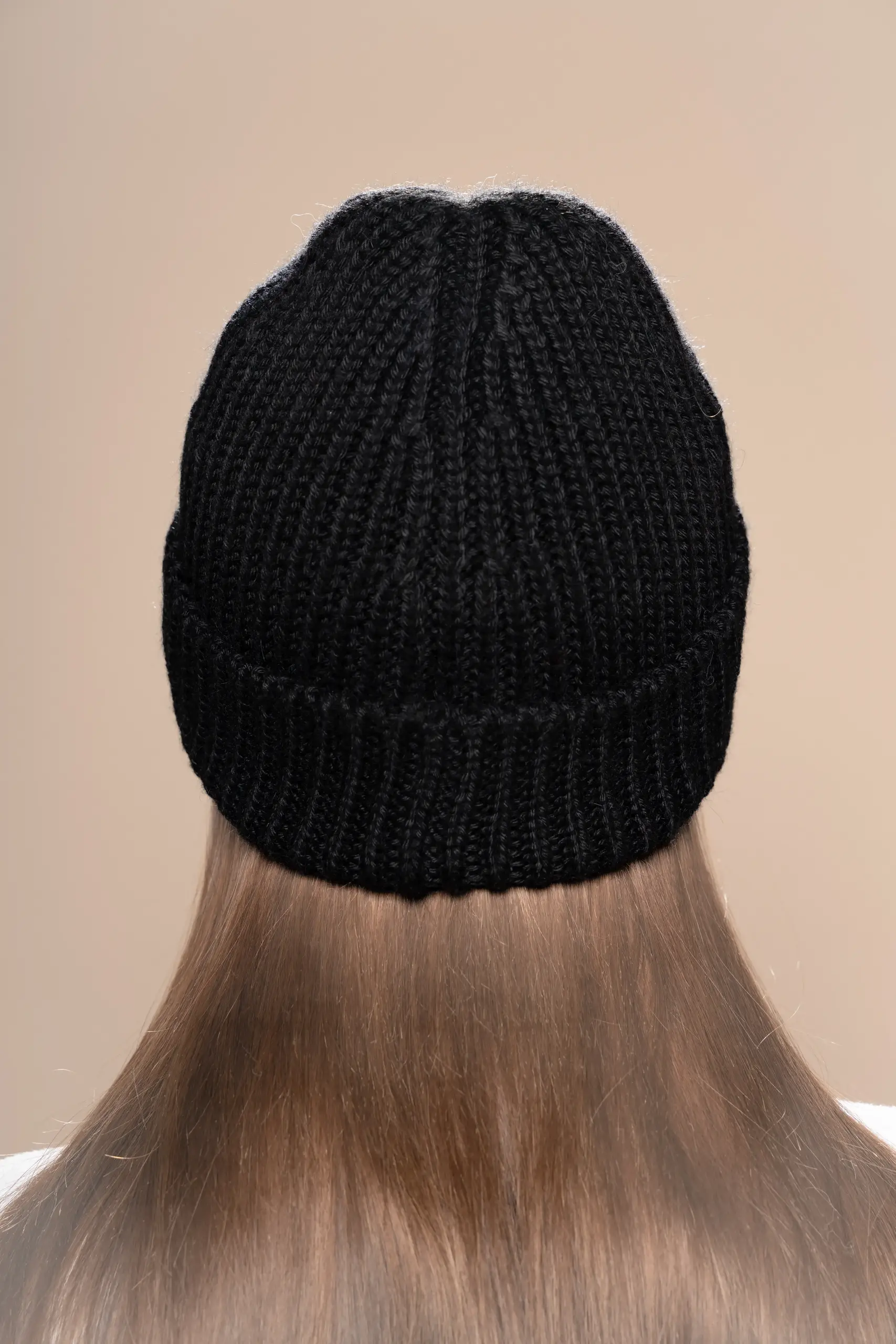 Woman wearing a black ribbed alpaca wool beanie from Tukuy, shown from back view against a neutral background.