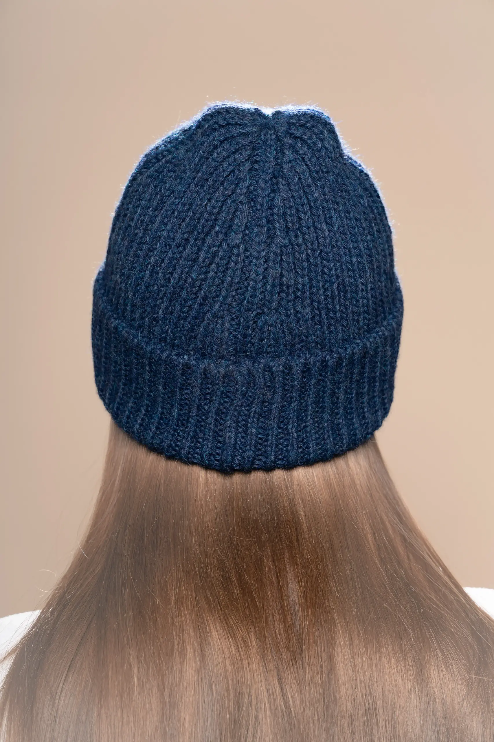 Woman wearing a blue alpaca beanie from Tukuy, shown from the back against a neutral background
