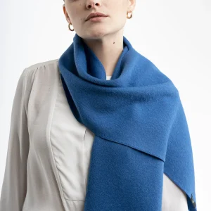 Woman wearing a blue alpaca scarf from Tukuy with fringed edges, styled over a white outfit against a neutral background.