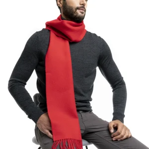 Man wearing a vibrant red alpaca wool scarf from Tukuy, styled over a dark turtleneck and grey trousers, seated against a white background.