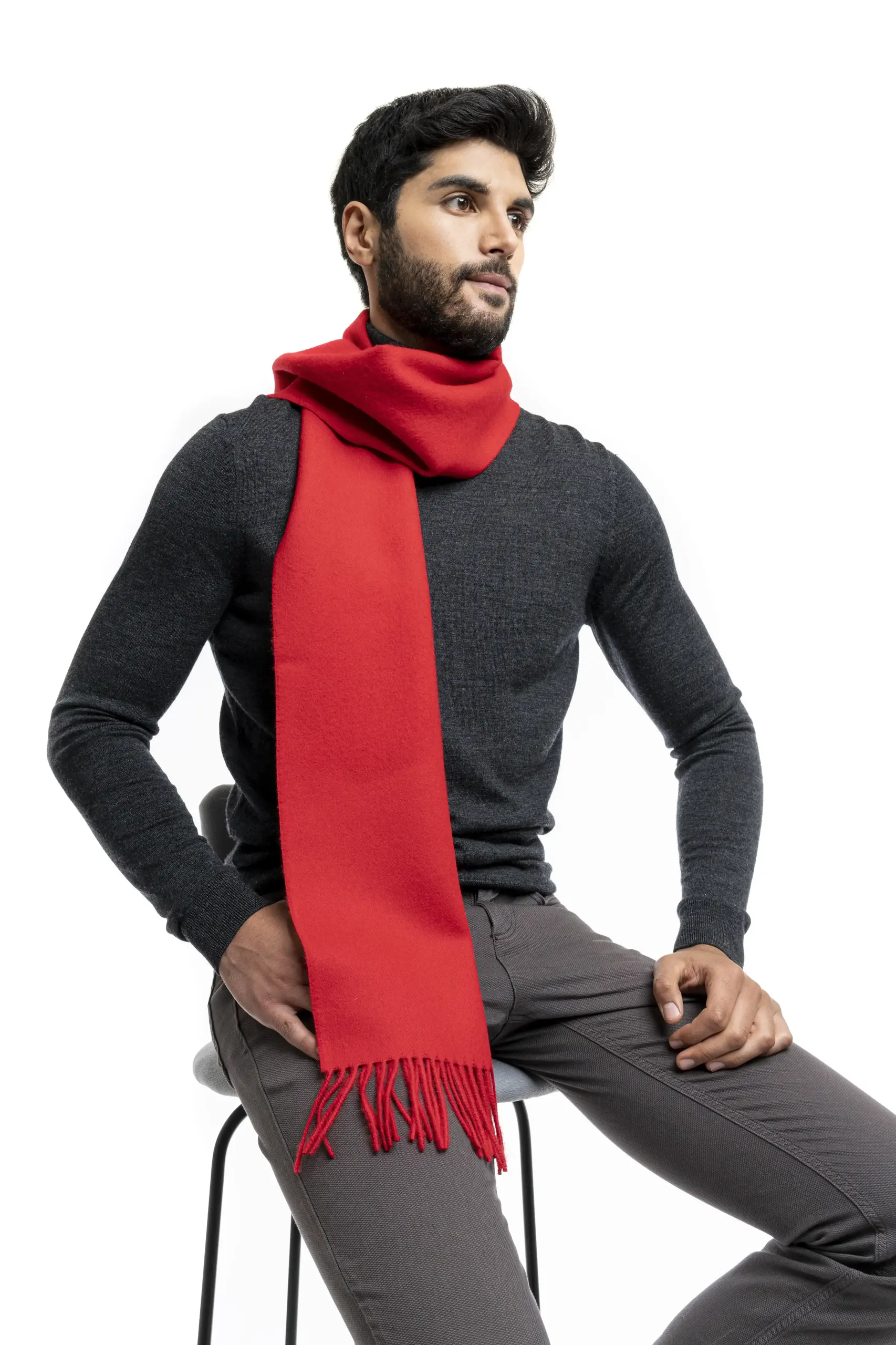 Man wearing a vibrant red alpaca wool scarf from Tukuy, styled over a dark turtleneck and grey trousers, seated against a white background.