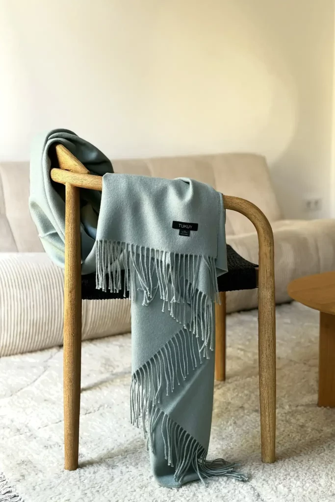 Green alpaca blanket from Tukuy draped over a chair in a cozy living room with a beige sofa