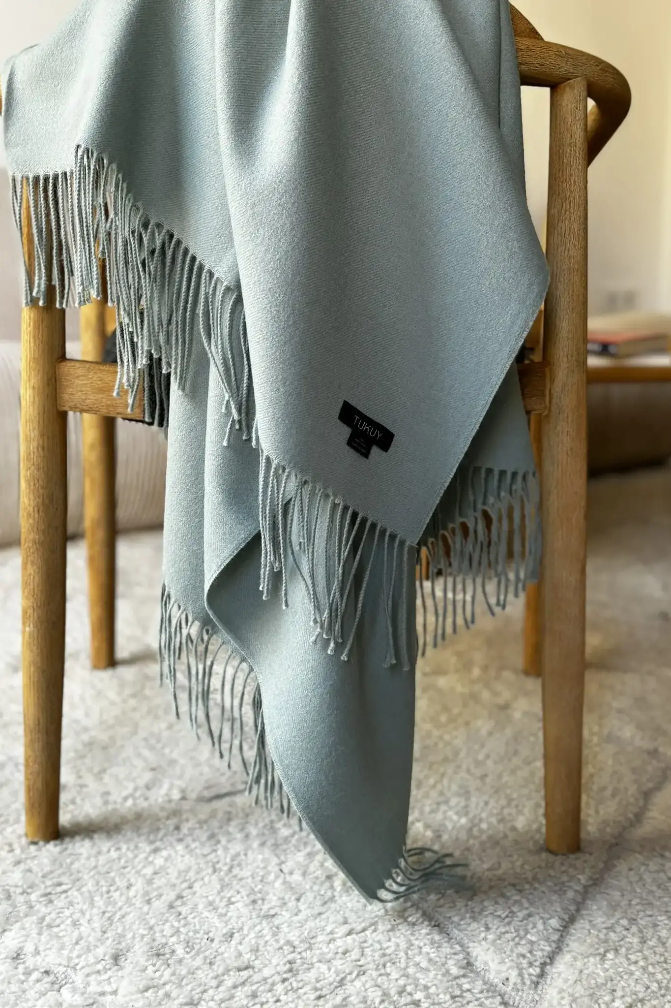 Close up of a green baby alpaca blanket from Tukuy draped over a chair in a cozy living room