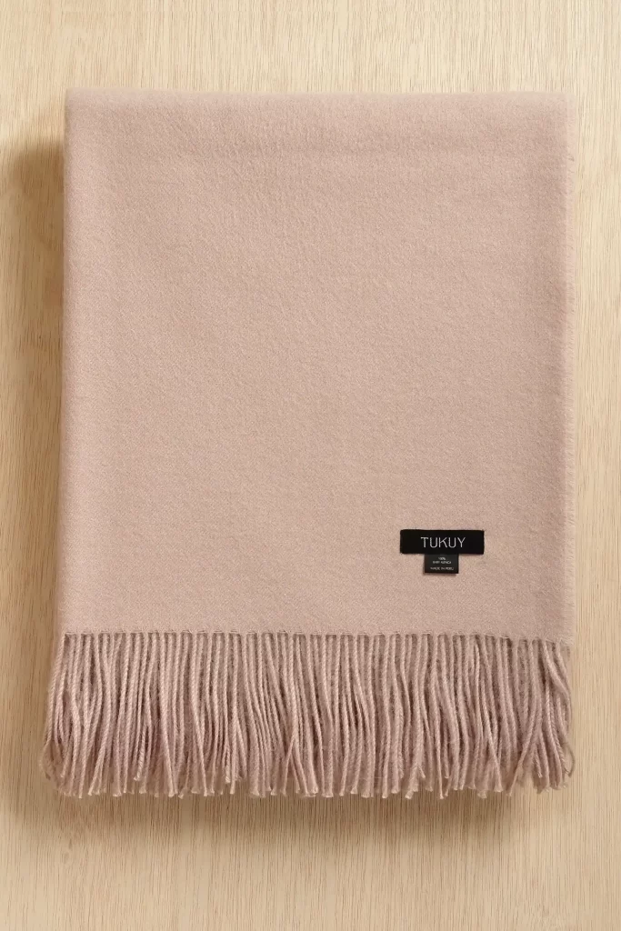 Pink alpaca wool blanket from Tukuy with fringe detail and woven label, soft pink and luxurious touch, placed on a wooden surface.