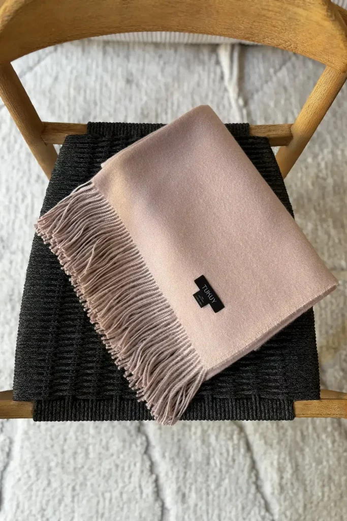 Manta de lana rosa claro baby alpaca de Tukuy colocada sobre una silla de madera en un salón moderno