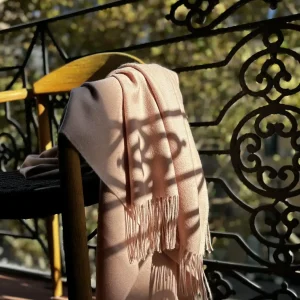 soft pink alpaca blanket from Tukuy draped over a wooden chair in a modern balcony in a sunny day