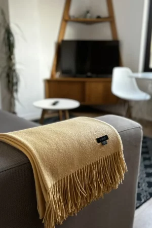 Yellow baby alpaca wool blanket from Tukuy draped over a sofa in a cozy living room