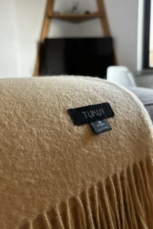 Yellow baby alpaca wool blanket from Tukuy draped over a sofa in a cozy living room