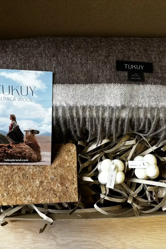 Gift box featuring a brown and beige baby alpaca wool blanket from Tukuy, paired with artisanal candles, a cork notebook, and a brand booklet. Perfect gift for her.
