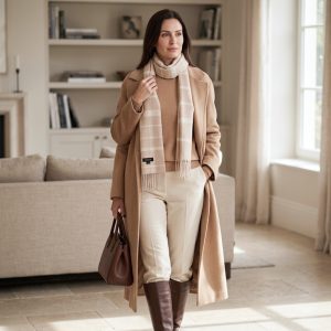 Woman wearing a beige check alpaca scarf with a camel coat, cream trousers, and brown boots, showcasing how the timeless checked pattern pairs beautifully with warm neutral tones.