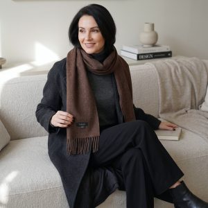 Una mujer que combina una bufanda de alpaca de color marrón chocolate con un abrigo gris carbón y unos pantalones oscuros, mostrando una elegante combinación de tonos neutros intensos y la suave textura de la lana de alpaca.