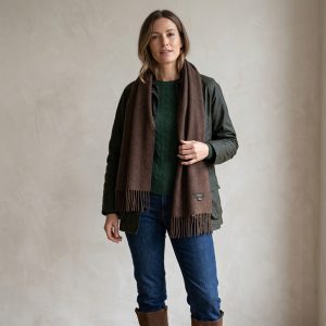 Una mujer lleva una bufanda de alpaca de color marrón chocolate con una chaqueta verde oliva y unos vaqueros azules, lo que demuestra cómo los tonos marrones intensos combinan a la perfección con los colores tierra para crear un look informal atemporal.