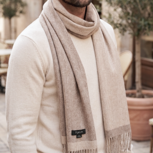 man wearing a reversible alpaca wool scarf in natural beige and taupe tones, paired with a cream sweater to showcase its soft texture and elegant drape.