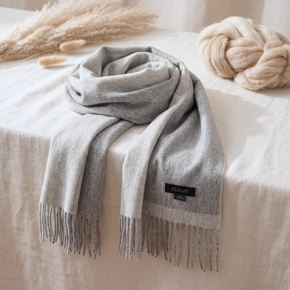 Reversible gray alpaca scarf displayed on a neutral linen surface, highlighting its natural gray color, luxurious softness, hand-finished fringes, and elegant reversible design.