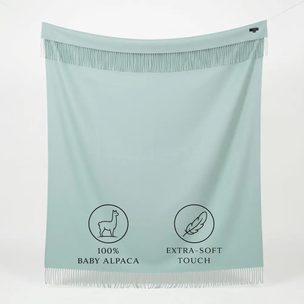 Baby alpaca blanket in pastel green with fringes hanging to display its full size and soft texture