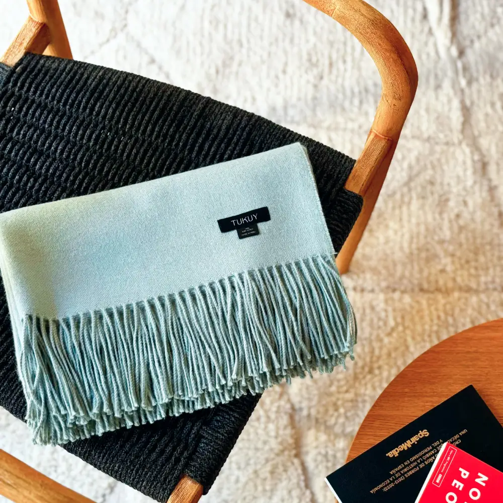 Soft baby alpaca blanket in pastel green draped over a chair showcasing its luxurious texture and fringe details