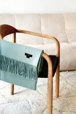 Baby green baby alpaca blanket draped over a wooden chair in a cozy modern living room