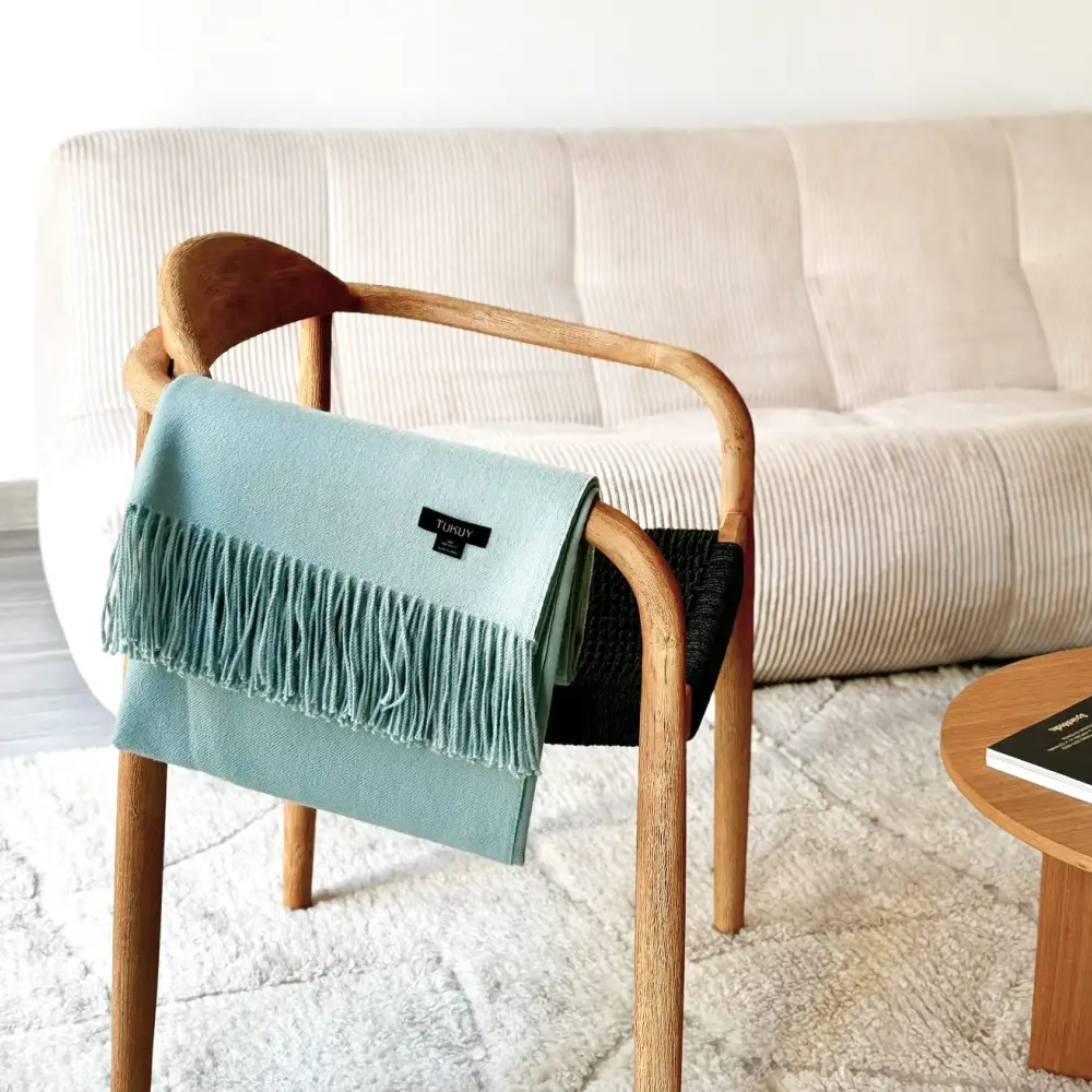 Baby green baby alpaca blanket draped over a wooden chair in a cozy modern living room
