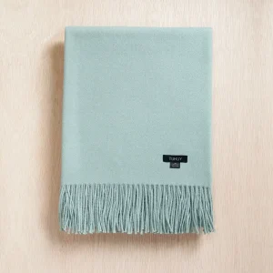 Baby green baby alpaca blanket folded on a neutral background with soft fringes