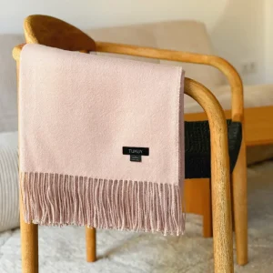 Baby pink baby alpaca wool blanket folded over a wooden chair – soft, warm Peruvian alpaca throw with elegant fringes