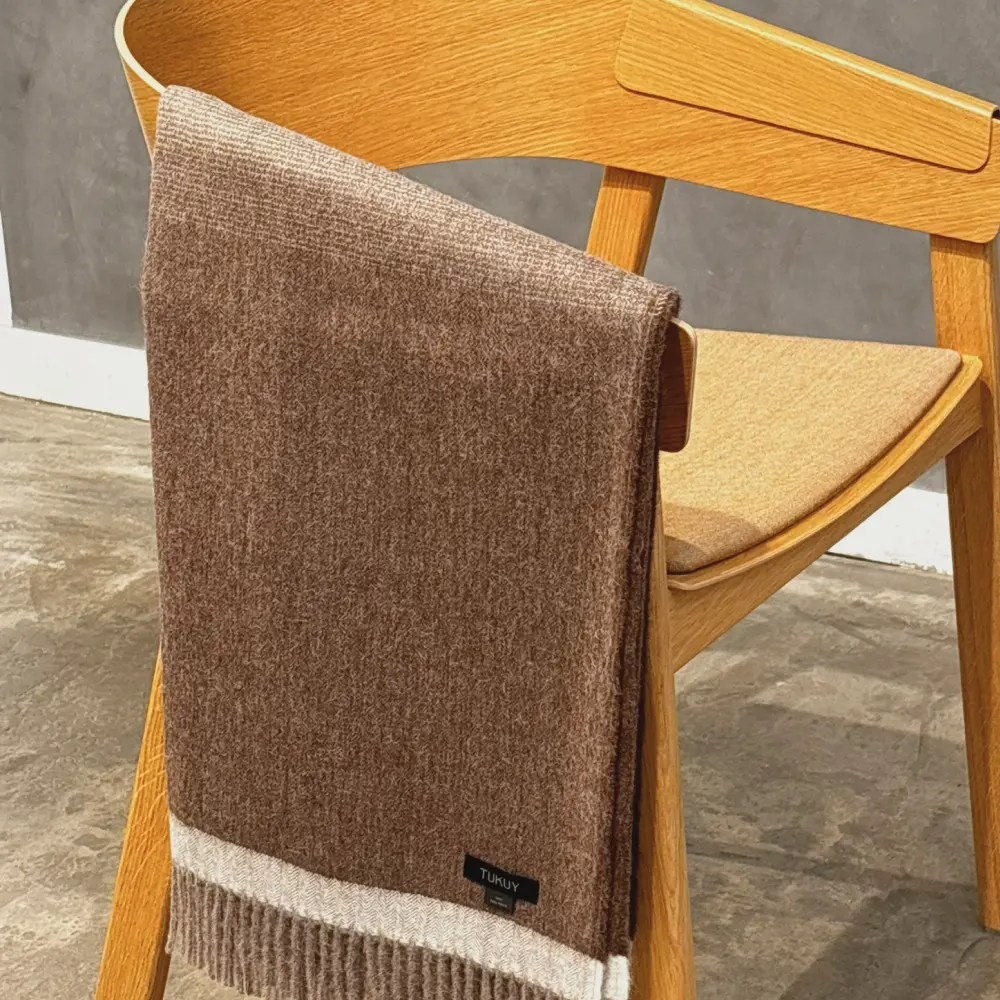 Baby alpaca blanket in brown folded over a wooden chair with fringe details
